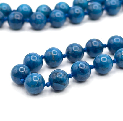 Extreme close macro of the strand doubling back on white, each round cobalt bead carrying a bright square highlight and the blue cord knots sitting tight between them.