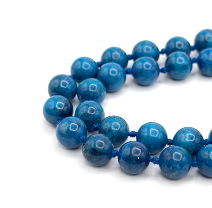 Macro of the strand's U-turn at the left, where the two rows meet in a rounded loop, the nearest cobalt beads and blue knots sharp and the back row falling softly out of focus.