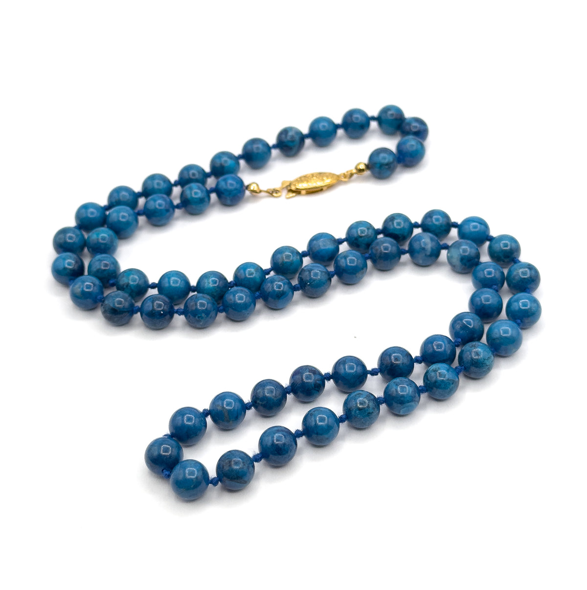 The whole necklace coiled into a long S on white, showing the full strand of cobalt beads doubling back on itself with the small oval yellow-toned clasp closed at the top.