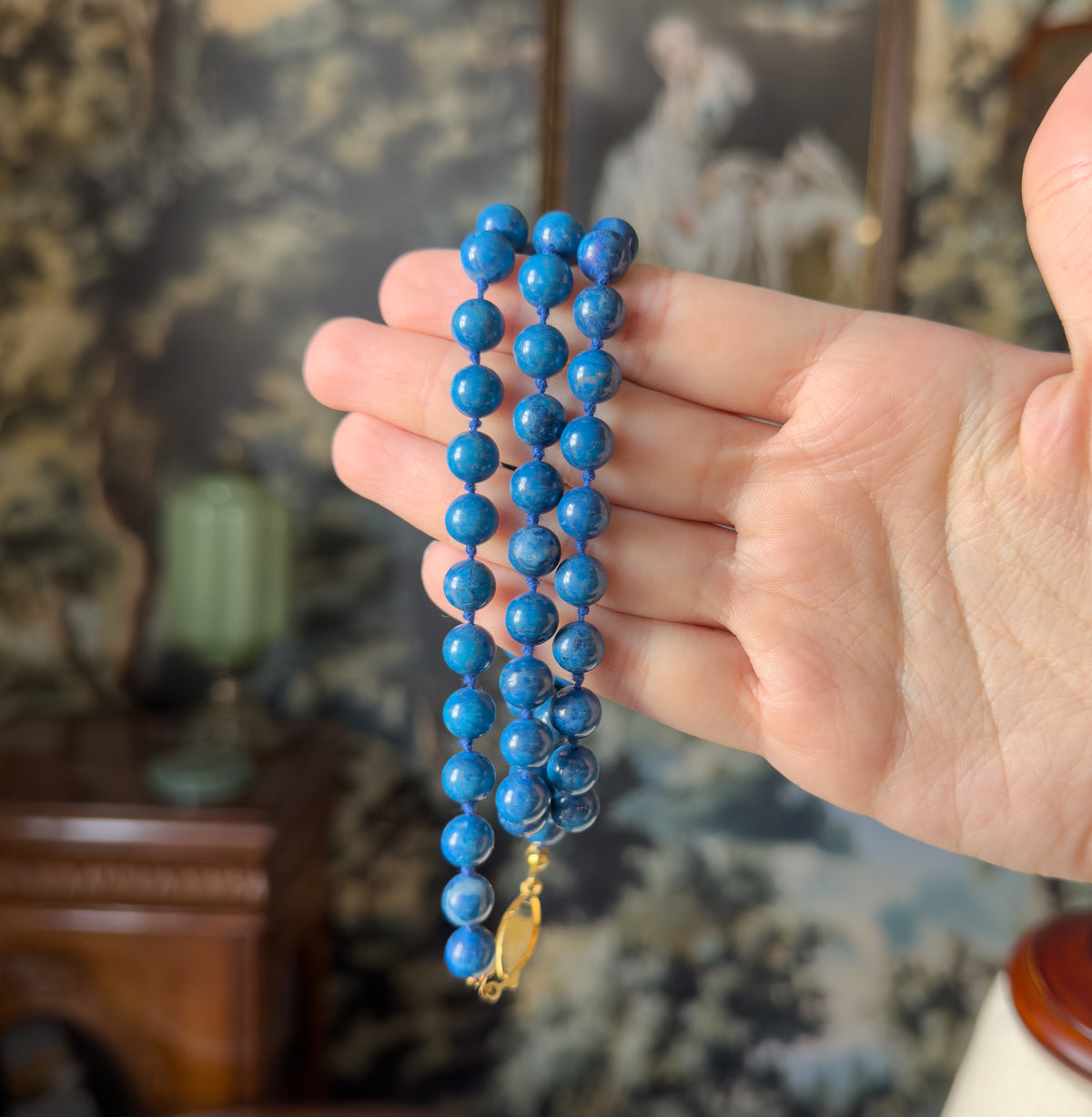 A vintage cobalt blue dyed quartz bead necklace, its knotted strand of round beads and small light-coloured clasp draped across an open palm, which gives a sense of its scale.