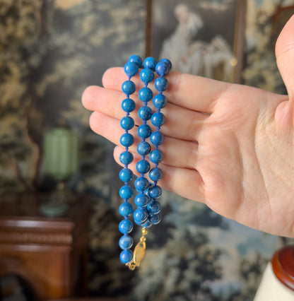 A vintage cobalt blue dyed quartz bead necklace, its knotted strand of round beads and small light-coloured clasp draped across an open palm, which gives a sense of its scale.