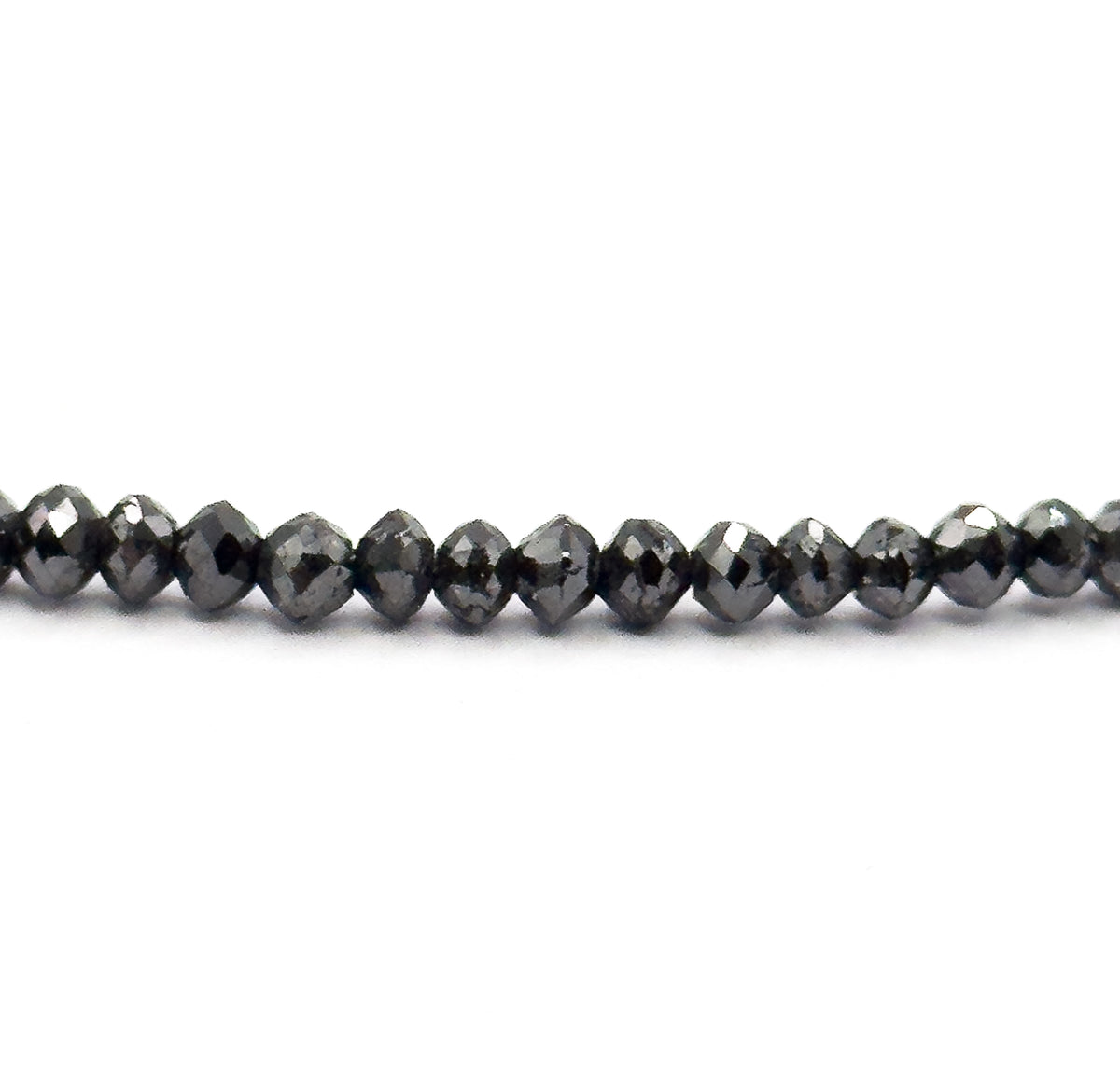 A straight horizontal run of the strand across white, seen edge-on so the faceted black diamond beads read as flattened rondelles with bright pinpoint highlights along their girdles.