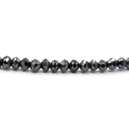 A straight horizontal run of the strand across white, seen edge-on so the faceted black diamond beads read as flattened rondelles with bright pinpoint highlights along their girdles.