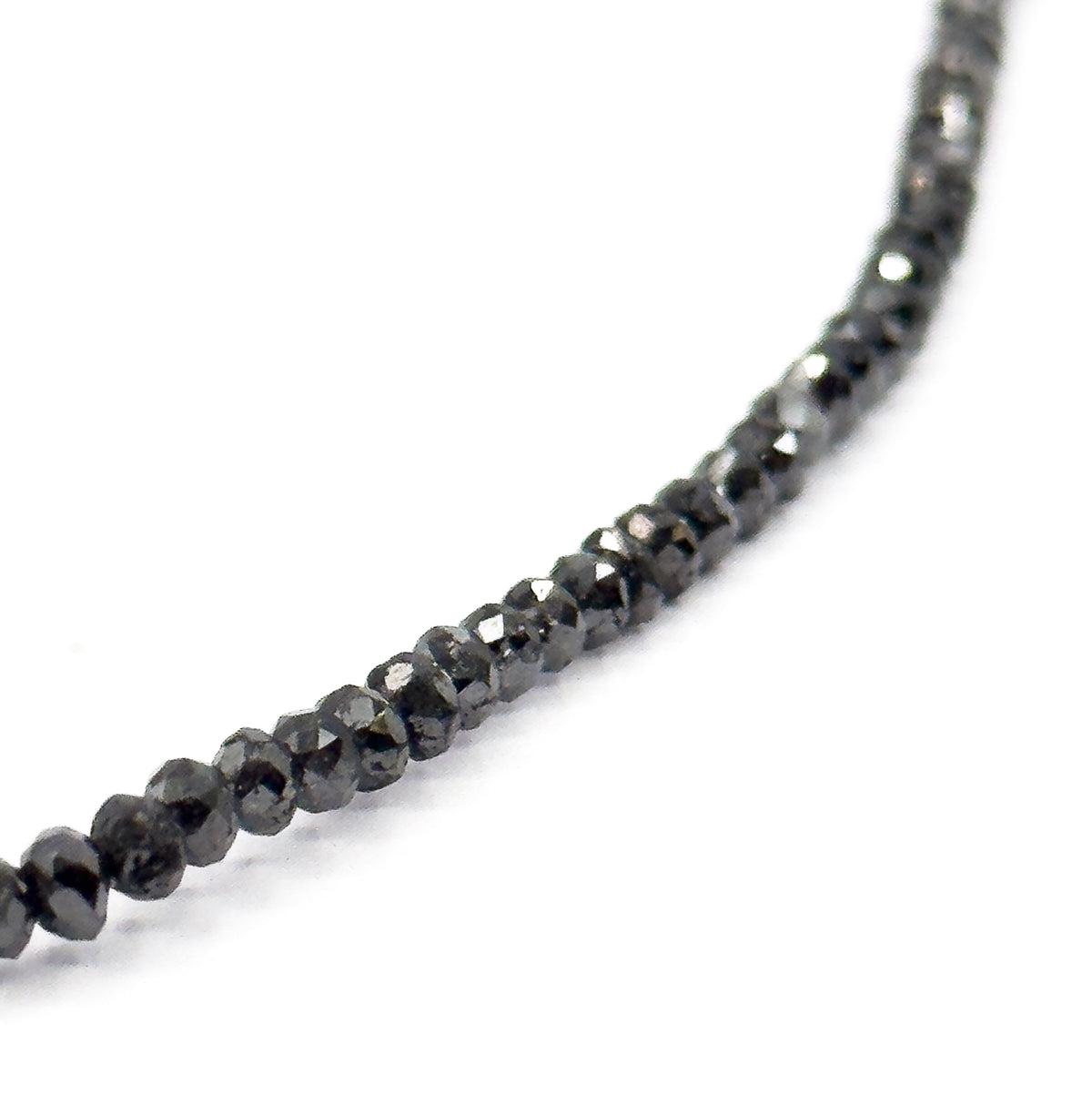 A diagonal length of the strand running from lower left into the upper right corner, the nearest faceted black diamond beads crisp while those further along soften into blur.