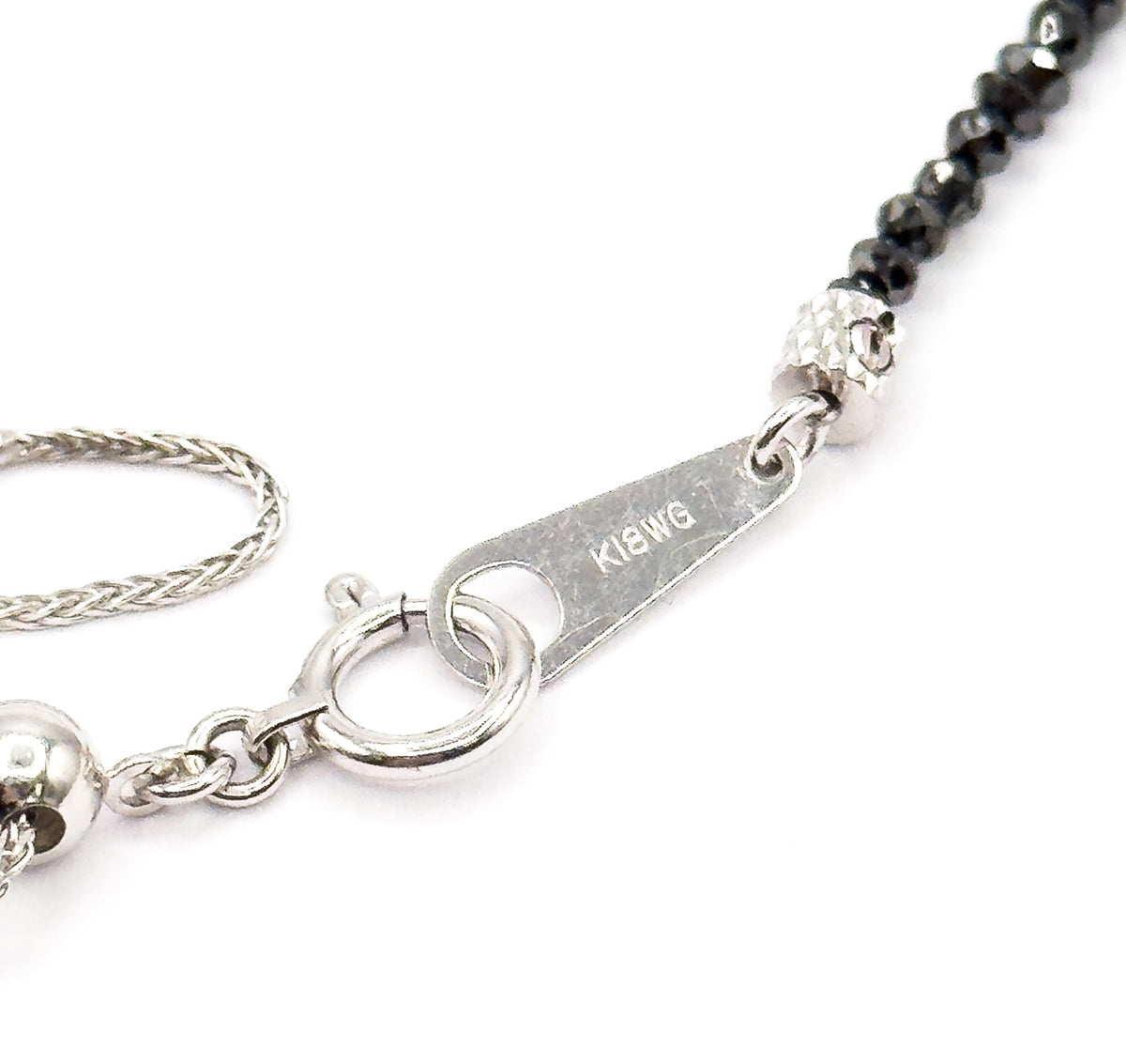 Close-up of the spring ring clasp and its small flat stamped tag linking the fine white gold chain to the first faceted black diamond beads at the end of the strand.