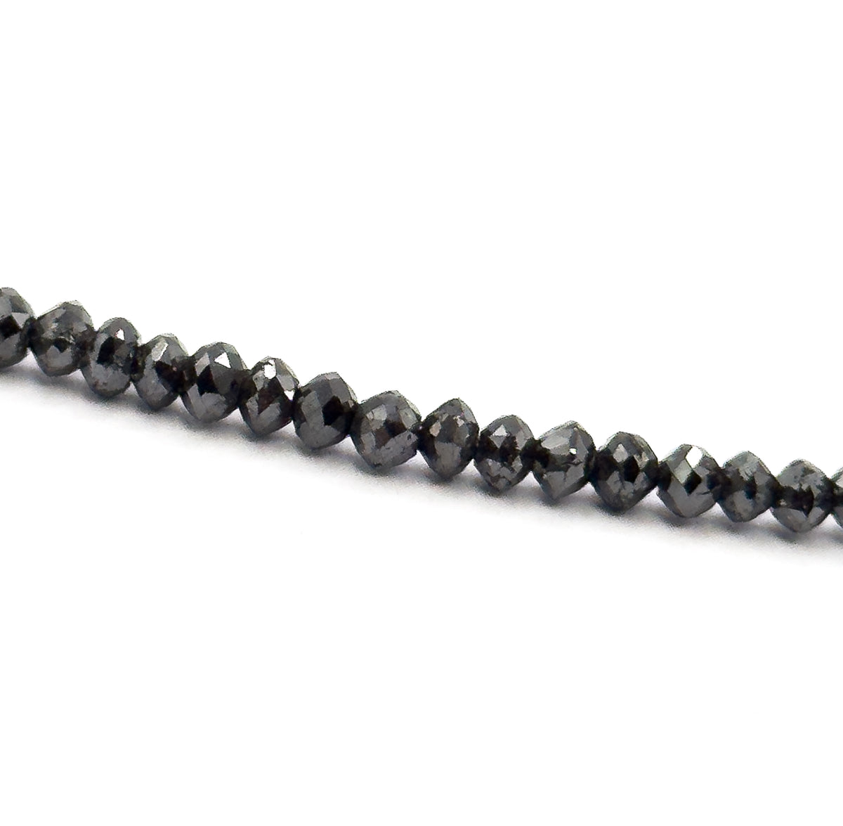 A tight macro of one diagonal section of the strand on white, each faceted black diamond bead sitting snug against the next, their small flat facets and graduated sizes clearly visible.