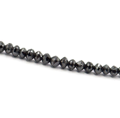 A tight macro of one diagonal section of the strand on white, each faceted black diamond bead sitting snug against the next, their small flat facets and graduated sizes clearly visible.