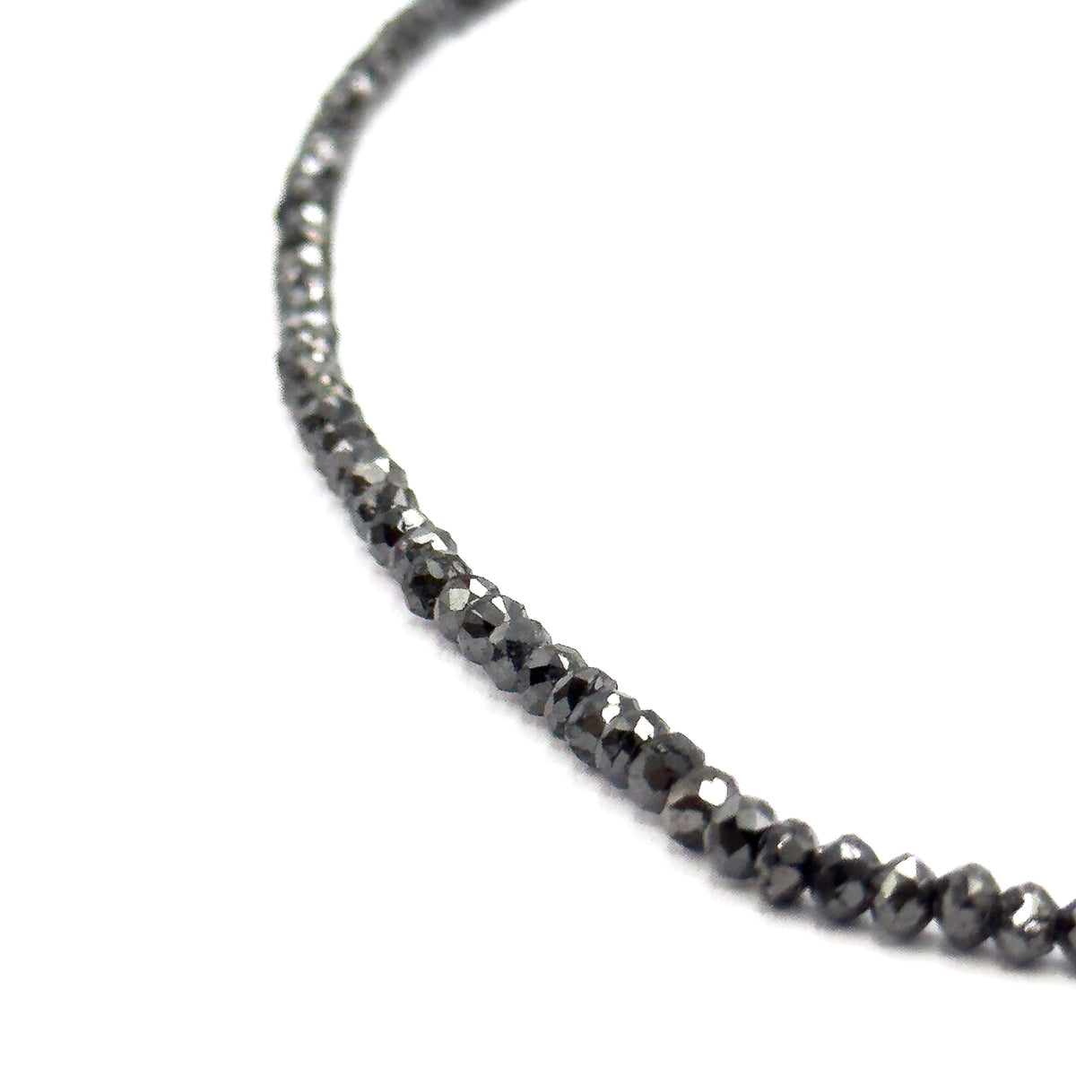 A sweeping arc of the strand curving across white, the beads tapering from tiny at the top to noticeably larger toward the bottom of the frame, showing the full graduation.