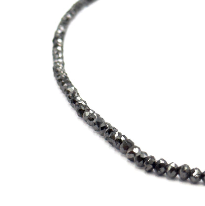 A sweeping arc of the strand curving across white, the beads tapering from tiny at the top to noticeably larger toward the bottom of the frame, showing the full graduation.