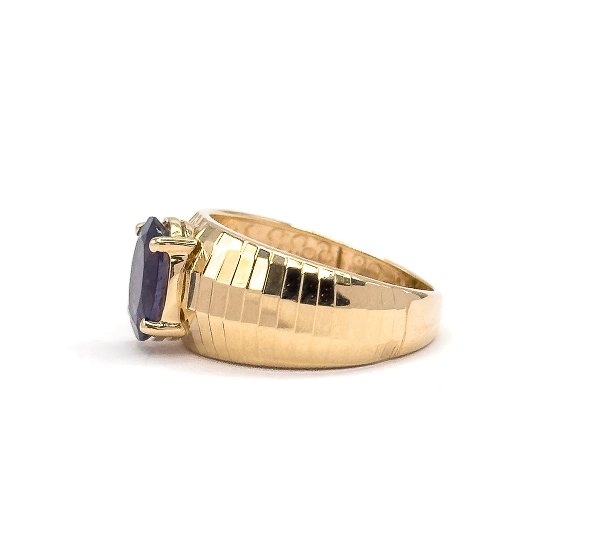 Side view from the opposite direction, the iolite at the left edge held between visible prongs, with the stepped faceted band sweeping right and the dimpled interior showing through the opening.