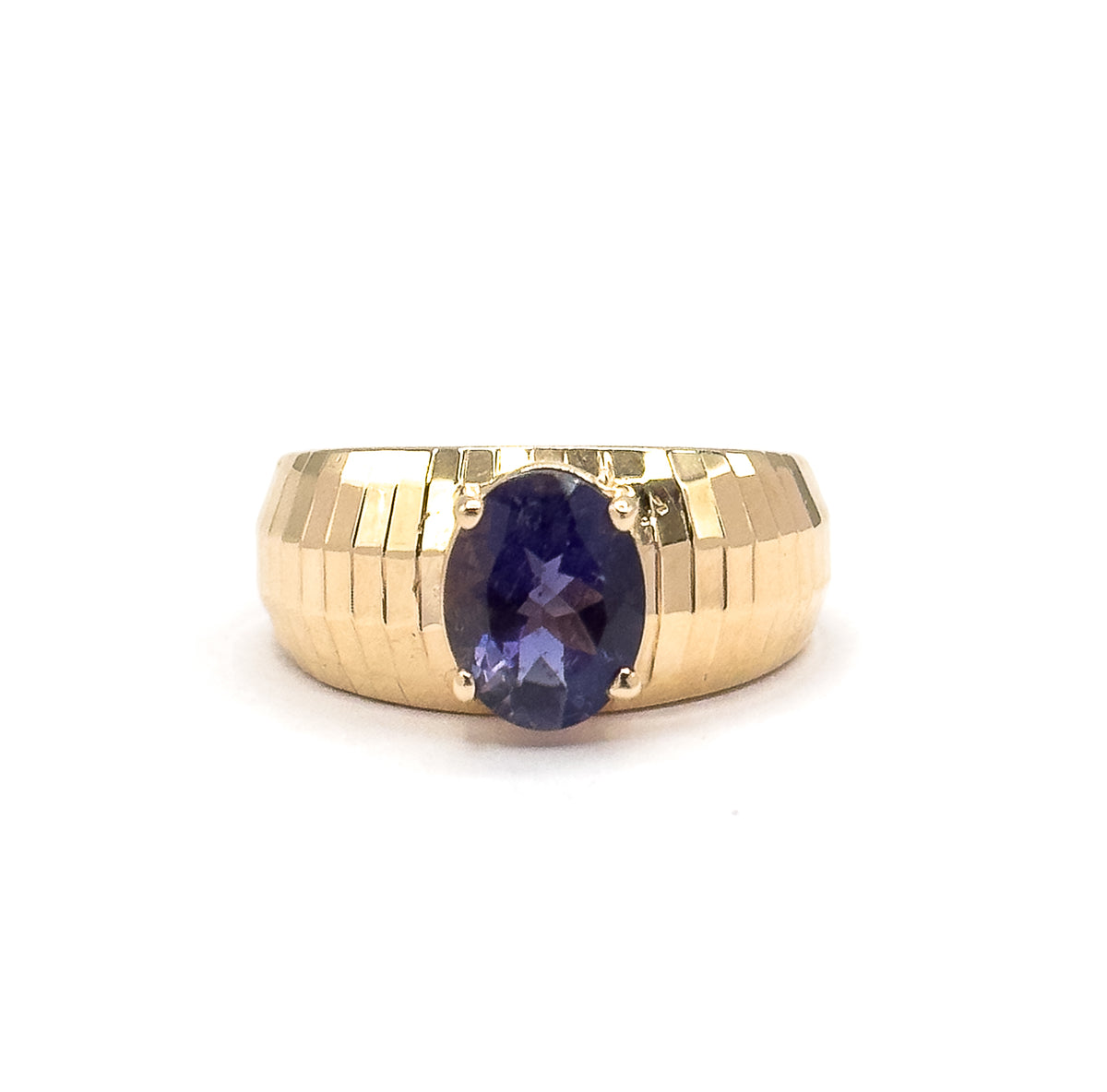 Straight-on close crop with the ring centred against plain white, the oval iolite upright between its four prongs and the stepped facets of the band tapering down toward the shank at each side.