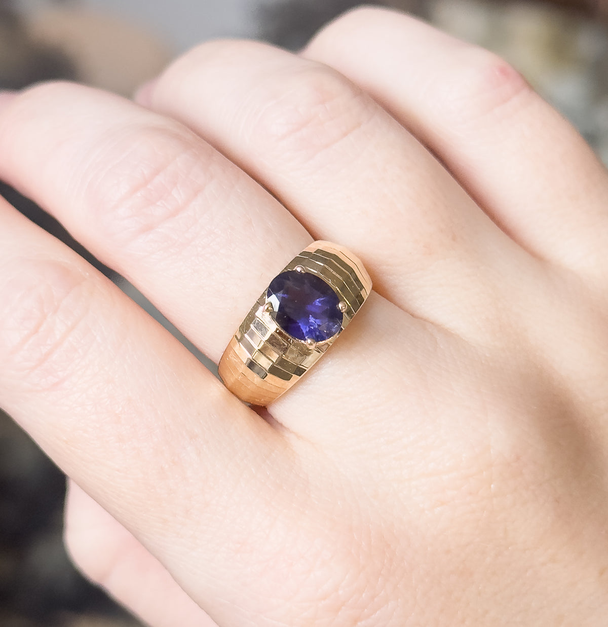 The ring shown on the hand from above with the fingers relaxed together, the oval iolite and its stepped yellow gold band small against the whole hand, giving a sense of scale.