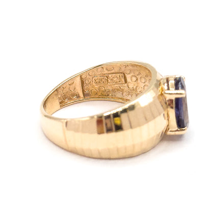 Rear view of the ring lying on its side, showing the patterned inside of the shank with its small stamped marks and the wide faceted yellow gold band, the iolite just visible at the edge.