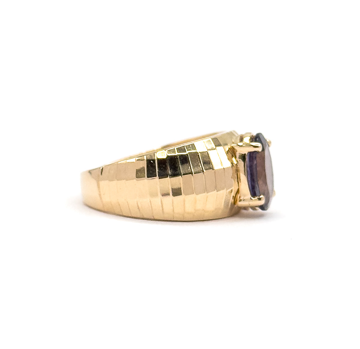 Profile view from the side, the wide yellow gold band filling the frame with its stepped facets and tapering shank, the prong-held iolite turned edge-on at the right.