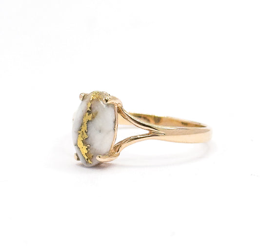 Profile view from the left, the marquise cabochon stands upright between its prongs with bright gold veining crossing the white stone, as the split shank sweeps back to the right.
