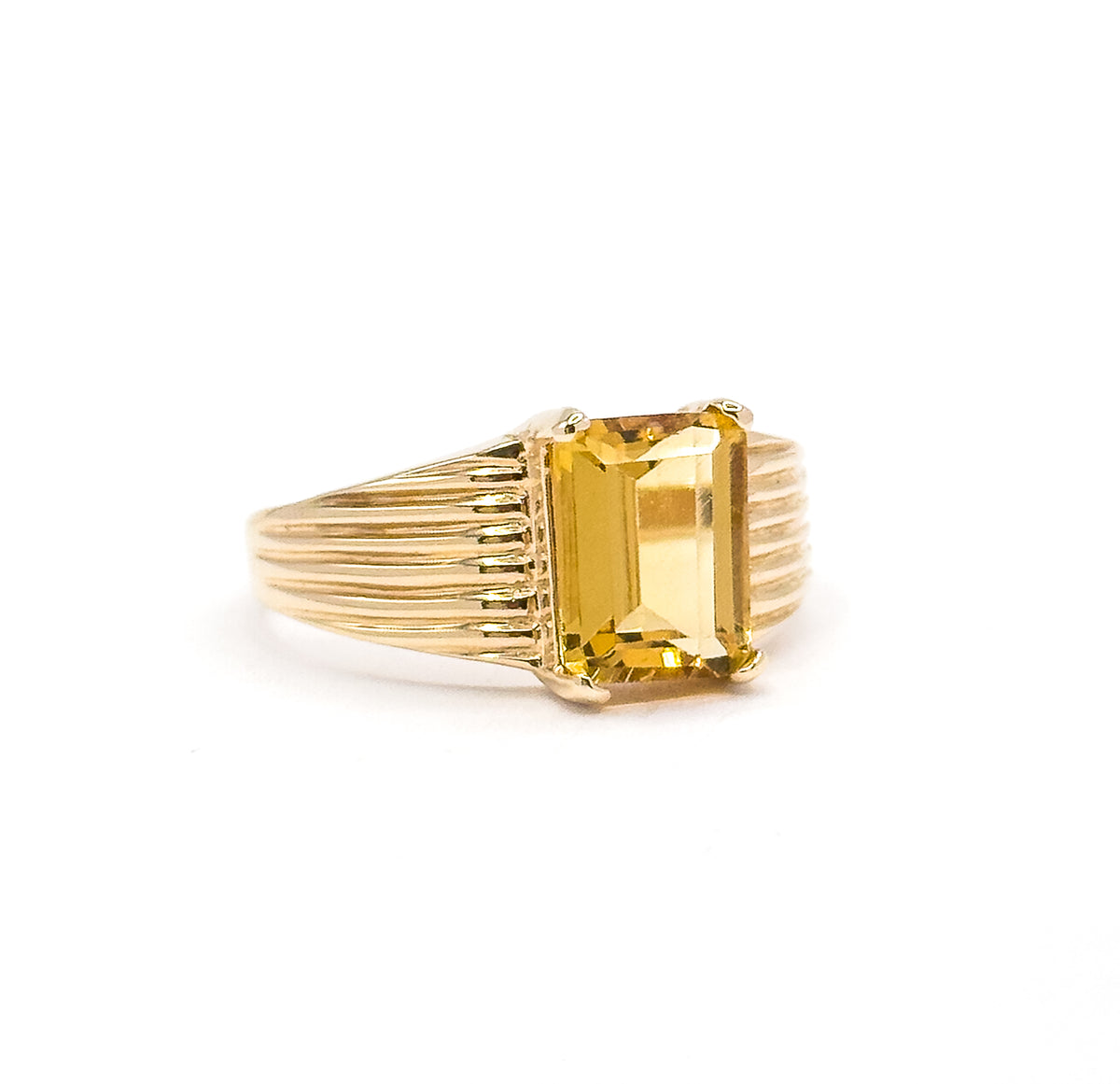 Off the hand against a white background, the ring stands upright in profile view, the citrine rising on prongs above the ribbed shoulders that narrow into the slim shank.
