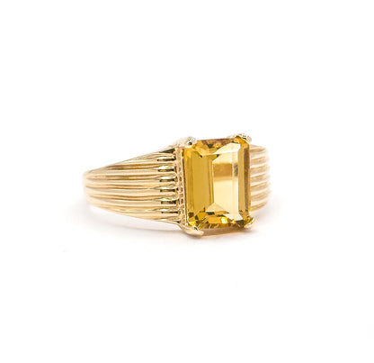 Off the hand against a white background, the ring stands upright in profile view, the citrine rising on prongs above the ribbed shoulders that narrow into the slim shank.