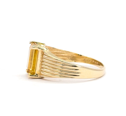 A straight side-on view from the opposite direction, the citrine's long rectangular side held by prongs at the face while the ribbed lines fan back along the shoulder into the smooth tapering shank.