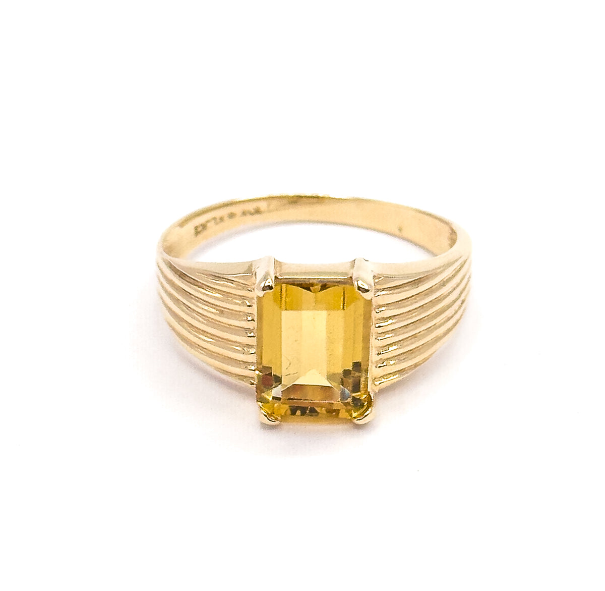 Seen face-on with the ring upright, the emerald-cut citrine's stepped rectangular table squared between four corner prongs as the ribbed shoulders flare out either side beneath the arched shank.
