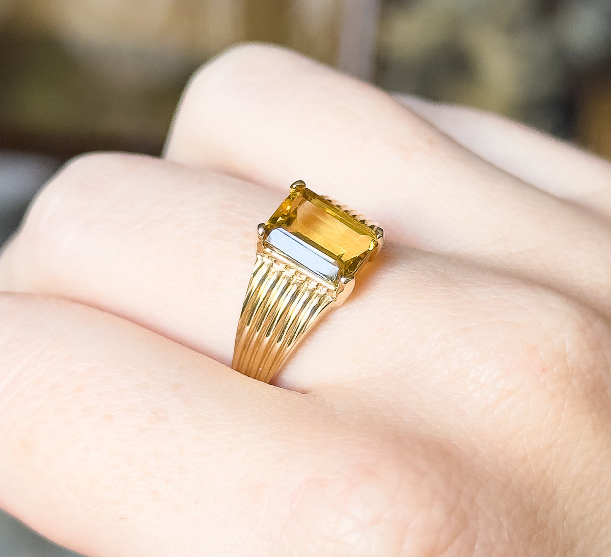An emerald-cut citrine ring in 10 karat yellow gold, shown on a finger, the prong-set golden stone raised above ribbed shoulders that taper to a slim shank.