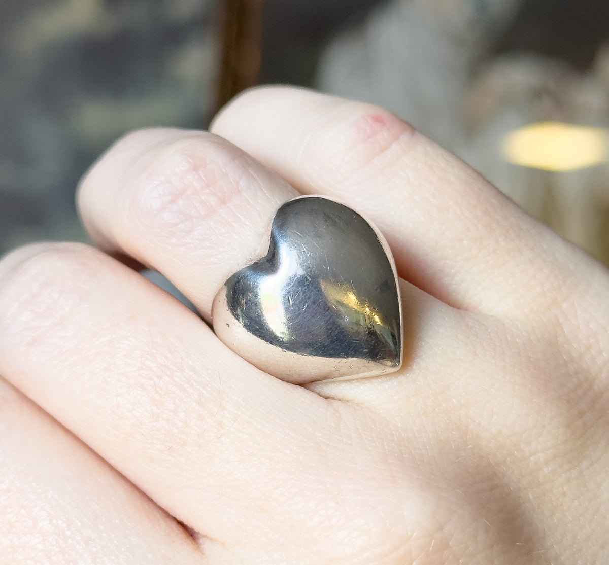 Almost the same view with slightly different angle, the heart tilted towards the camera so its domed surface catches a warm highlight, the finger filling the frame for scale.