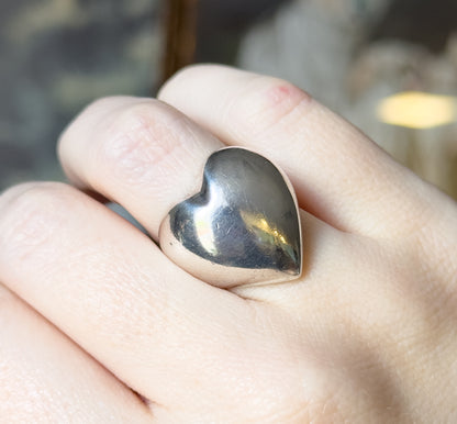 Almost the same view with slightly different angle, the heart tilted towards the camera so its domed surface catches a warm highlight, the finger filling the frame for scale.