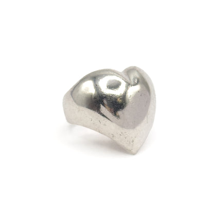 Off the hand now against a plain white background, the ring stands upright so the full domed heart face and the narrow shank curving beneath it are visible.