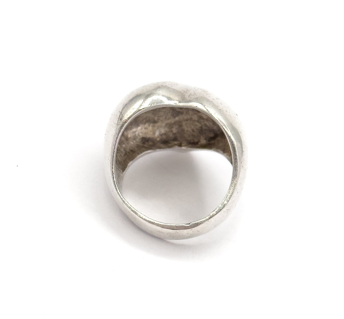 Seen from behind against white, the open circle of the shank frames the hollow underside of the domed heart, showing how the band widens as it rises.