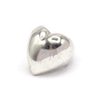 Close in on the heart face alone against white, the polished sterling dome fills the frame with bright highlights across its rounded lobes and the shank tucked out of sight behind.