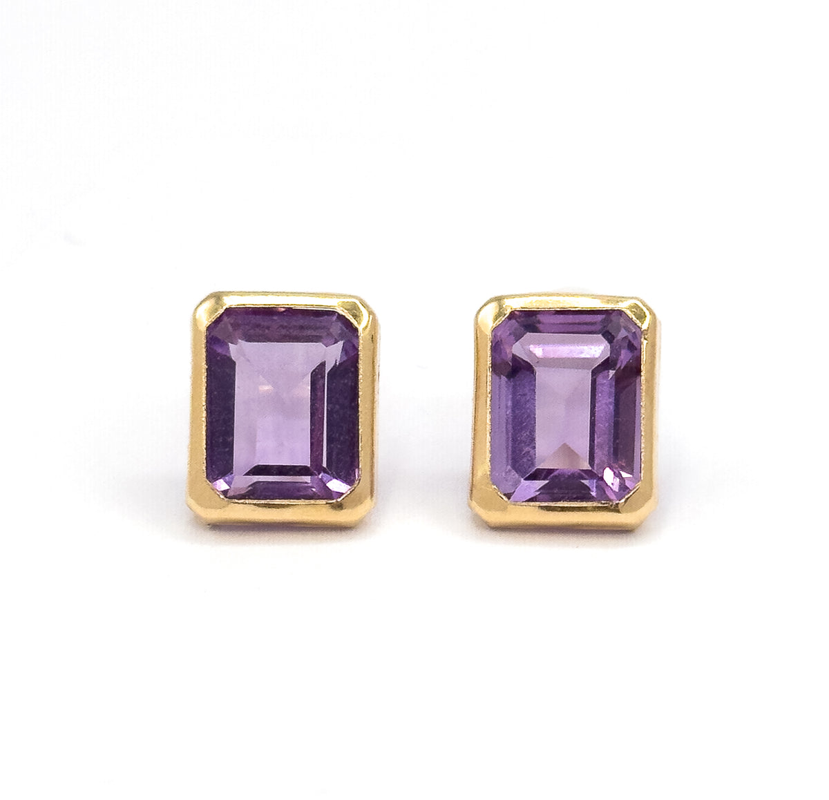 Almost the same view with slightly different angle, cropped closer so the cut corners of each yellow gold bezel and the broad central facet down each purple amethyst fill the frame.
