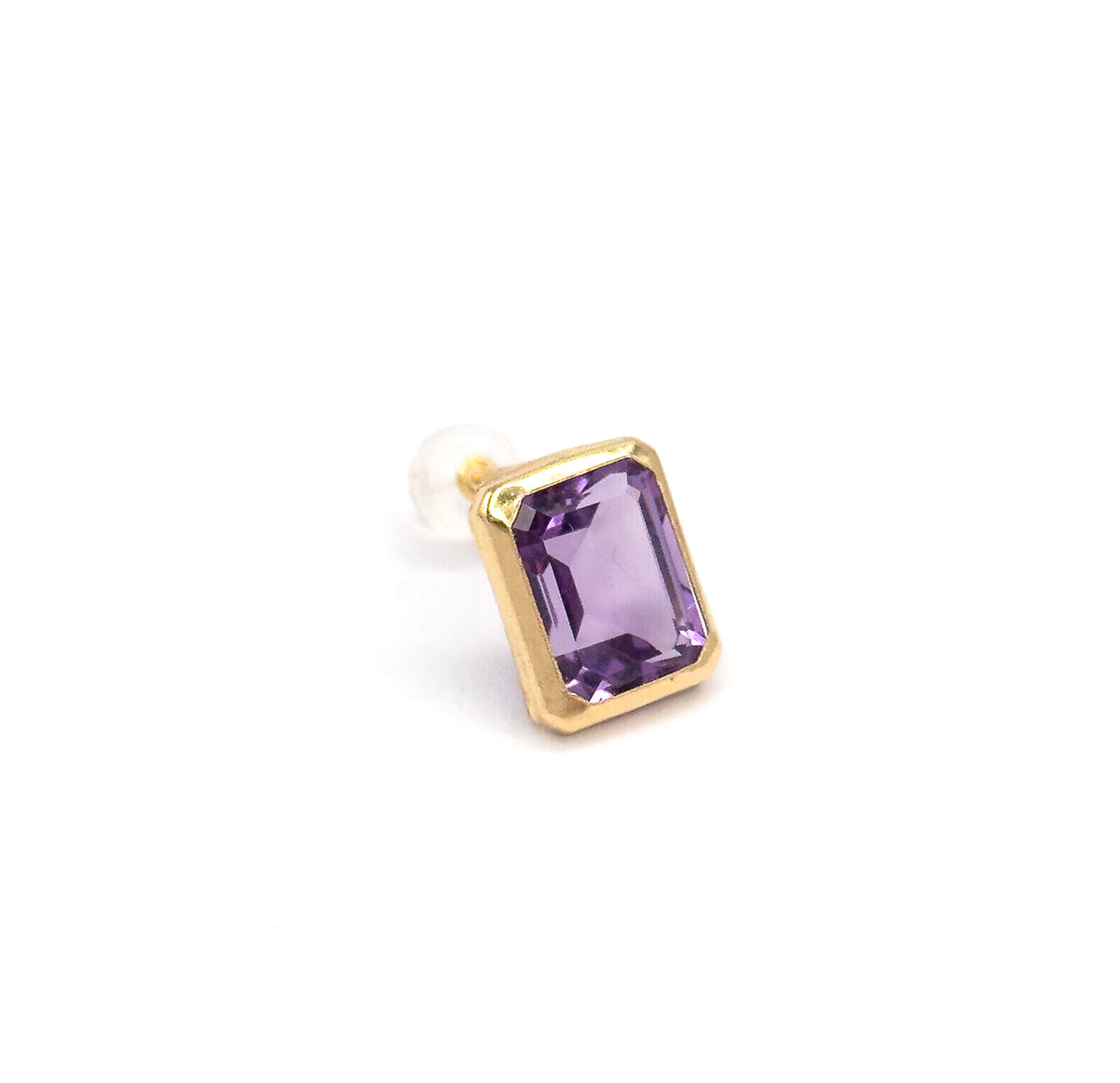 A single stud shown at an angle against white, the emerald-cut amethyst in its yellow gold bezel tilted forward with the post and clear backing visible behind.