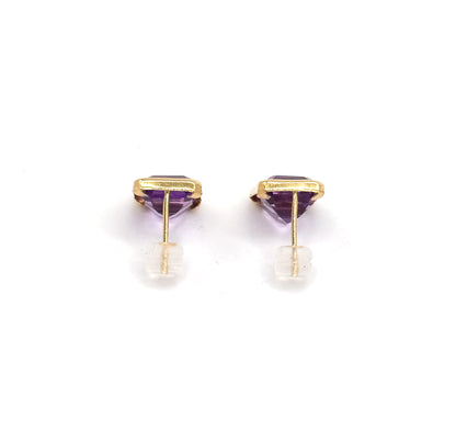 Both studs side by side from behind, the yellow gold bezels seen edge-on with the pointed purple stones below and each post threaded through a clear backing.