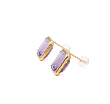 Both studs overlapping in a diagonal line against white, the posts angled to the right with their clear backings spaced apart, so the stepped faceting across both purple stone faces is visible.