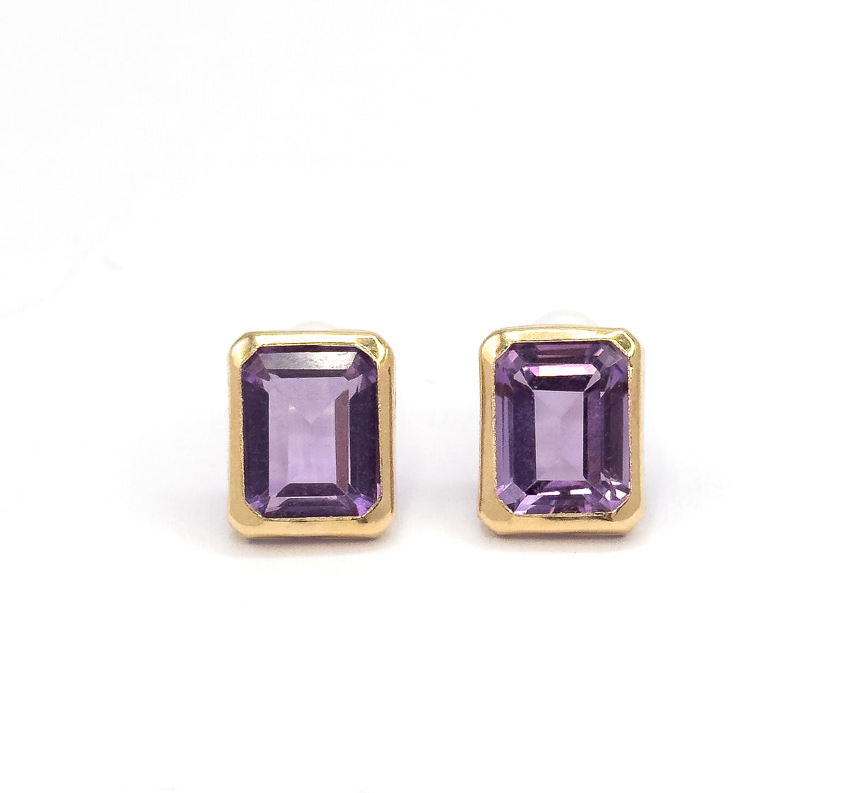 Both studs upright and side by side, square-on to the camera against white, so the yellow gold bezels and the stepped facets of each purple amethyst are seen straight on.