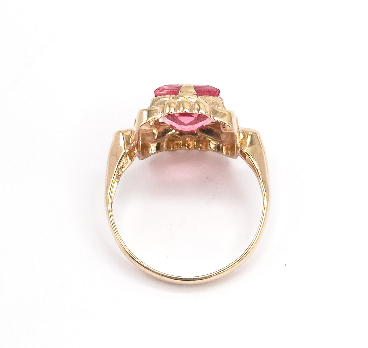Viewed from the back with the open circle of the shank facing the camera, the gallery and underside of the setting are visible, the pink glass showing between the scalloped yellow gold prongs.