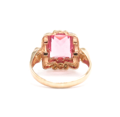 Standing with the shank arching below, the setting is seen from behind and slightly above, the pink glass glowing through the open scalloped frame with beaded accents at its top and base.