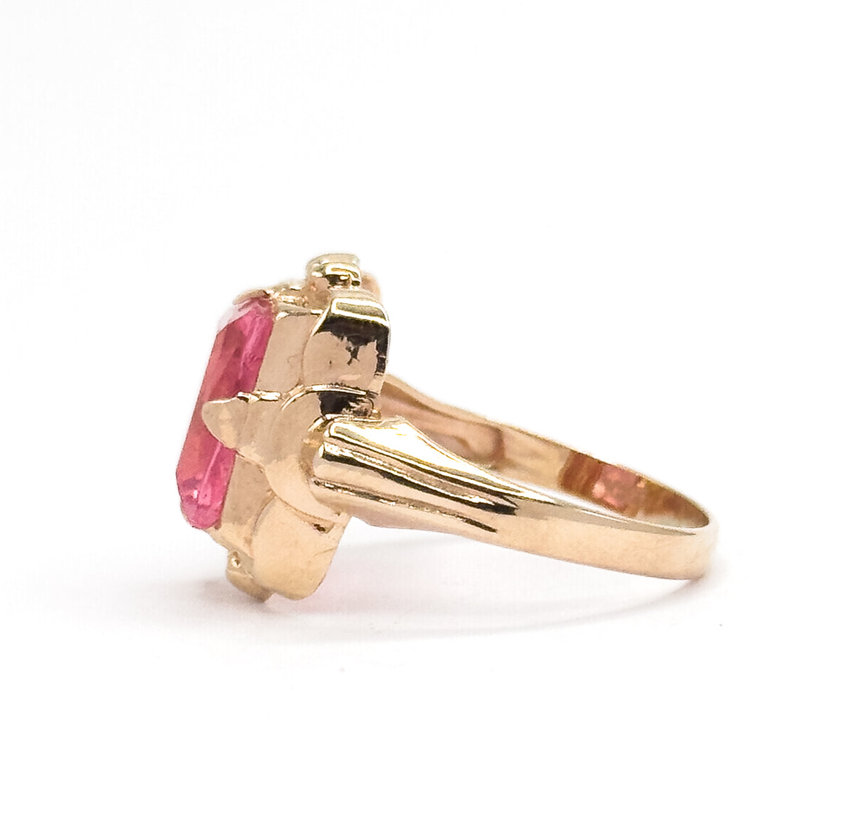 Seen from the opposite side with the shank sweeping to the right, the grooved yellow gold shoulders and the squared edge of the pink glass stone sitting low in its bezel are in clear view.