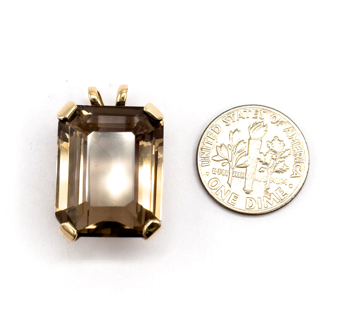 Shown beside a dime for scale, the pendant lies face up with its bail at the top, the emerald-cut smoky quartz slightly taller and wider than the coin in its four yellow gold prongs.
