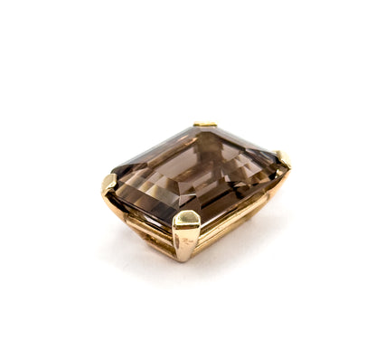 A three-quarter view from above and in front, the golden brown stone tilted so its table and crown facets show while the smooth yellow gold gallery wall curves along the lower edge between two corner prongs.