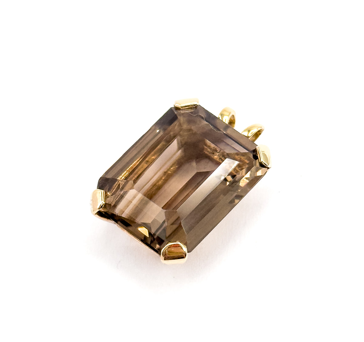 Angled from above with the bail tipped away to the upper right, all four yellow gold corner prongs are visible gripping the emerald-cut smoky quartz against the white ground.