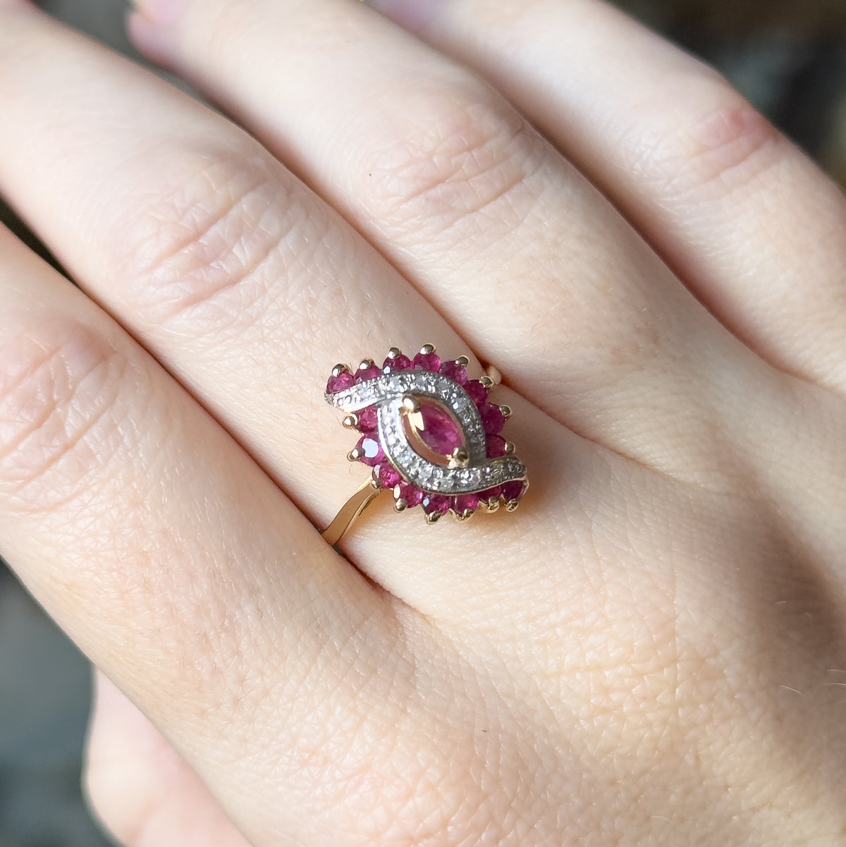 Closer view on the hand from above, the wavy marquise face set across the finger so the prongs holding each round ruby and the slim yellow gold shank are clearly visible.