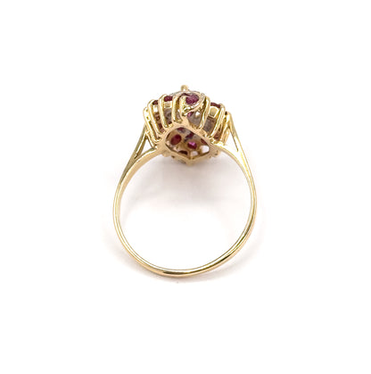 Standing upright on a white background, seen from behind so the open gallery, split shoulders and the full round of the slender yellow gold shank are visible beneath the ruby-set head.