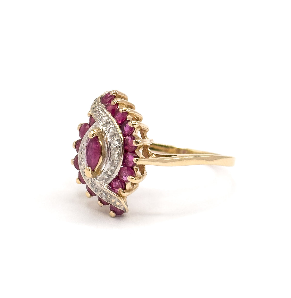 Angled three-quarter view from the side, the marquise ruby and white gold waves facing left while the prong tips over the outer round rubies and the tapering yellow gold shank sweep away to the right.
