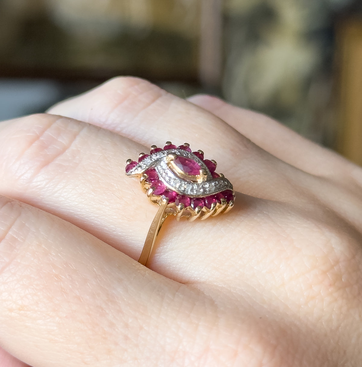 Ruby and diamond waterfall ring in two-tone 10 karat gold, shown on a finger, its marquise ruby ringed by round rubies and diamond accents on a white gold face above a yellow gold shank.