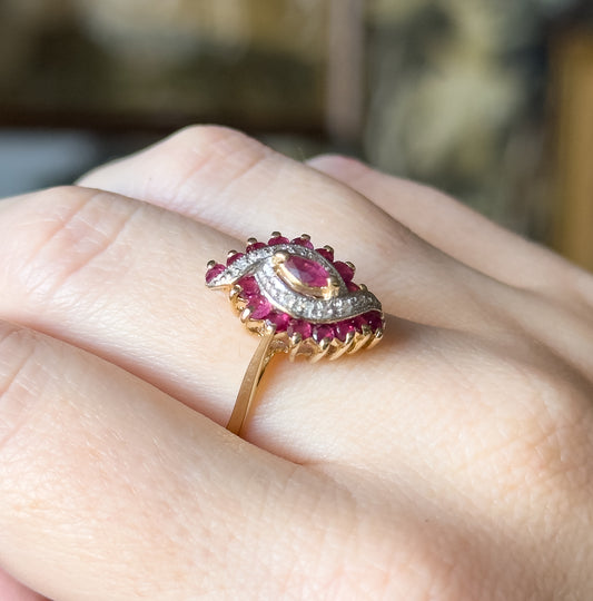 Ruby and diamond waterfall ring in two-tone 10 karat gold, shown on a finger, its marquise ruby ringed by round rubies and diamond accents on a white gold face above a yellow gold shank.