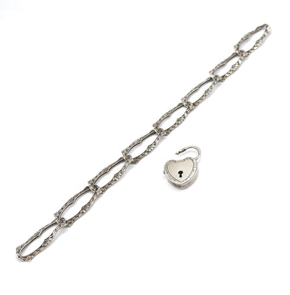 The full bracelet laid out straight on a diagonal, every elongated floral link visible end to end, with the heart-shaped lock clasp detached and open to one side.