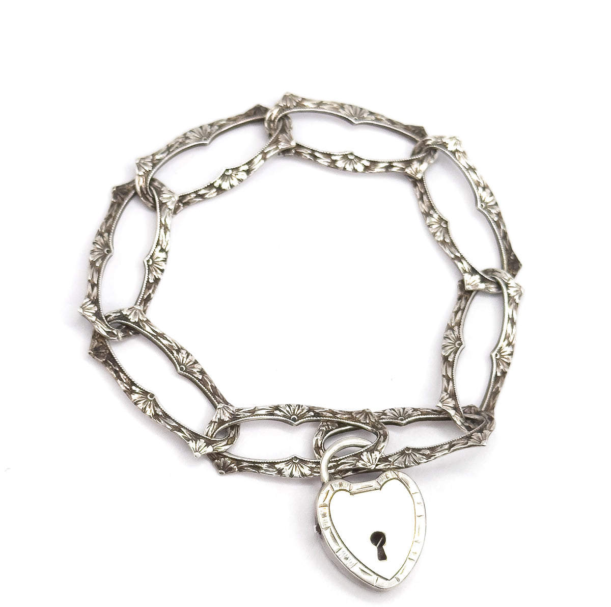 Seen from directly above as a closed oval circle, every elongated link's fan-shaped floral engraving is visible in turn, with the heart-shaped lock clasp hanging at the bottom edge.