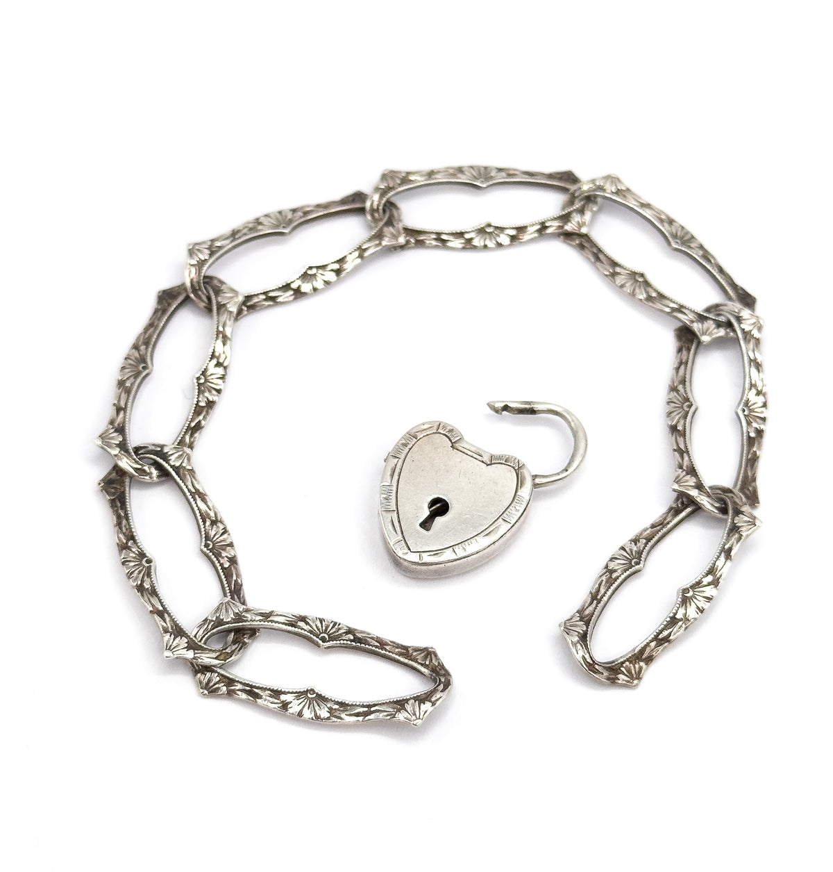 The bracelet curves in an open arc with the heart-shaped lock unclasped and detached inside it, its hooked shackle swung up and the keyhole on the plain face in full view.