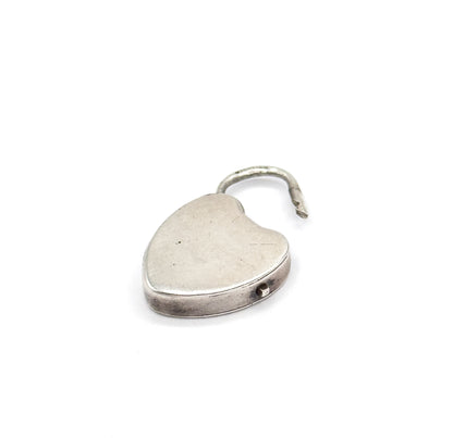 Close-up of the heart-shaped lock on its own, shackle swung open above the plain smooth face, with a small pin visible in the banded rim along the lower edge.