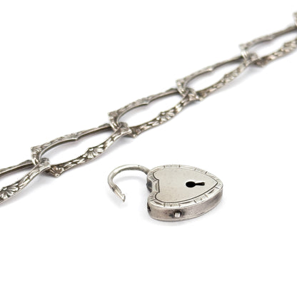 Steep diagonal view along the chain of elongated links, their milgrain edges and floral motifs receding into the distance, with the open heart lock resting below at the near end.